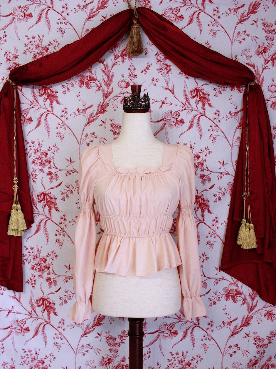 Historically Inspired Renaissance Smocked Blouse with Juliet Puff Sleeves in Peachy Pink, in front of a toile backdrop.