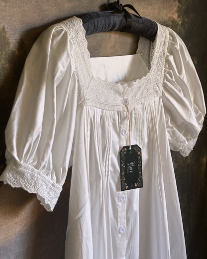A historically inspired regency style short sleeve chemise dress with pin-tuck pleats and lace trim in front of an art history backdrop