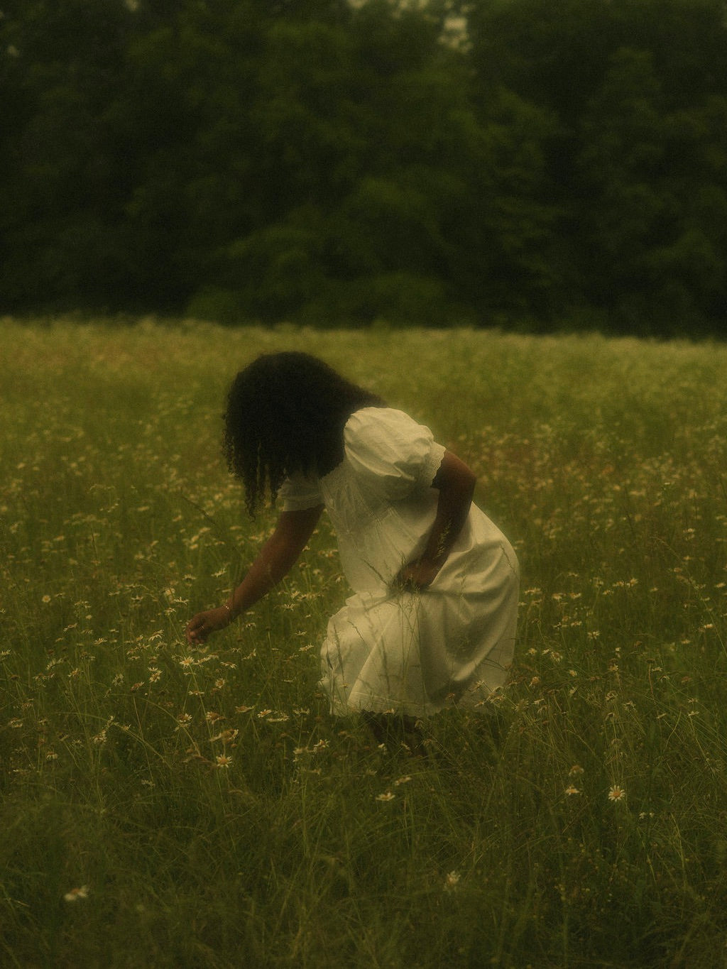 A woman in a flower field wearing a vintage style historically-inspired white short-sleeve chemise dress with lace trim, puff sleeves, and pleated details.