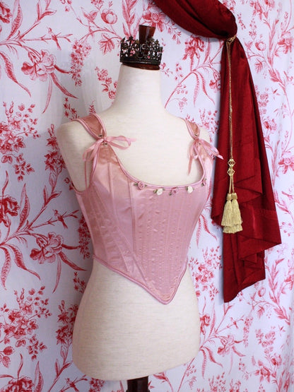 A pair of Balletcore Renaissance, Baroque, Rococo, Regency, Victorian Era Corset Stays in Ballet Pastel Pink with Rosette Appliques in front of a toile backdrop.