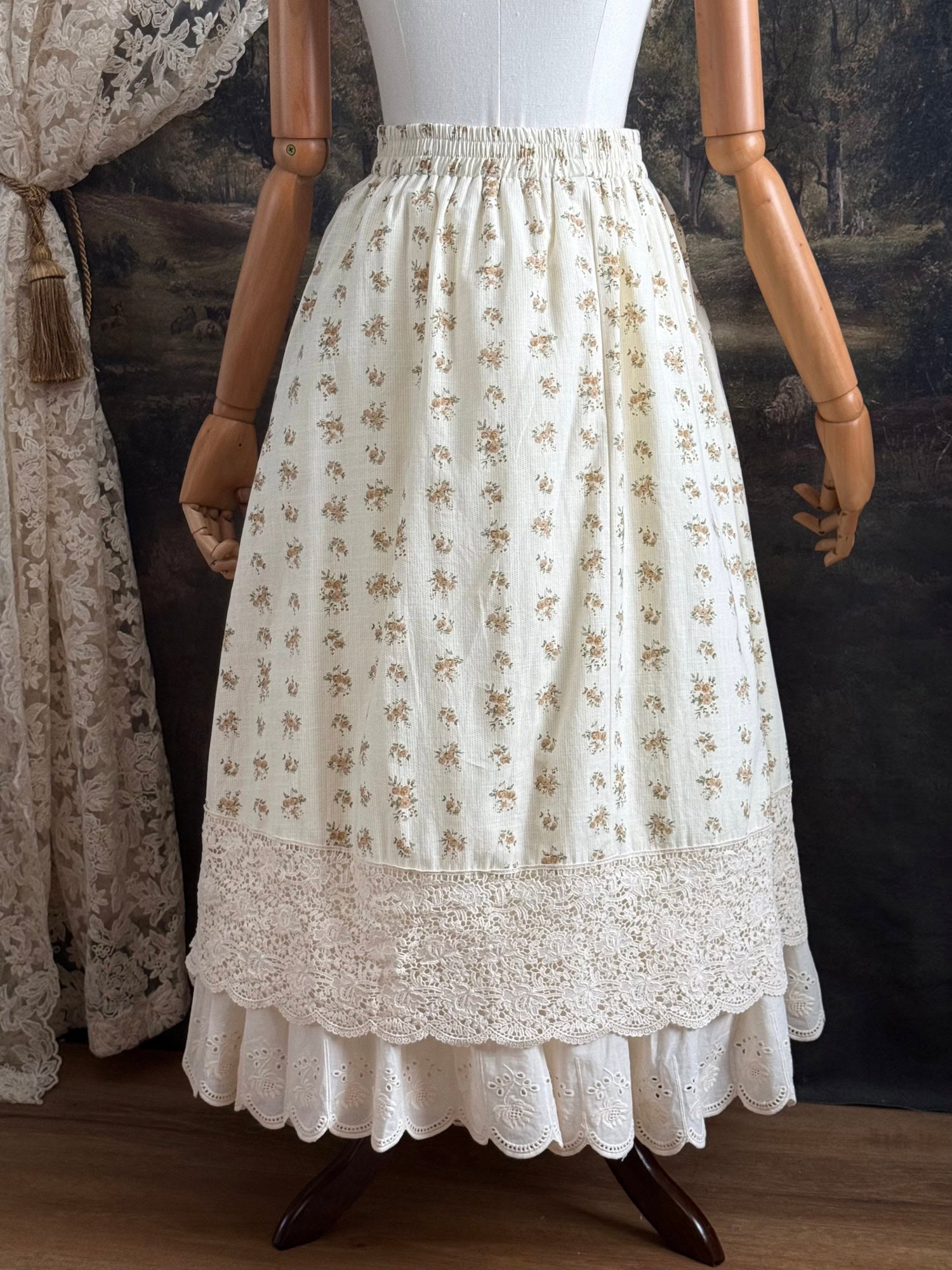 A historically inspired victorian style Ivory cotton floral printed maxi skirt with scalloped lace trim on a mannequin in front of an art history backdrop