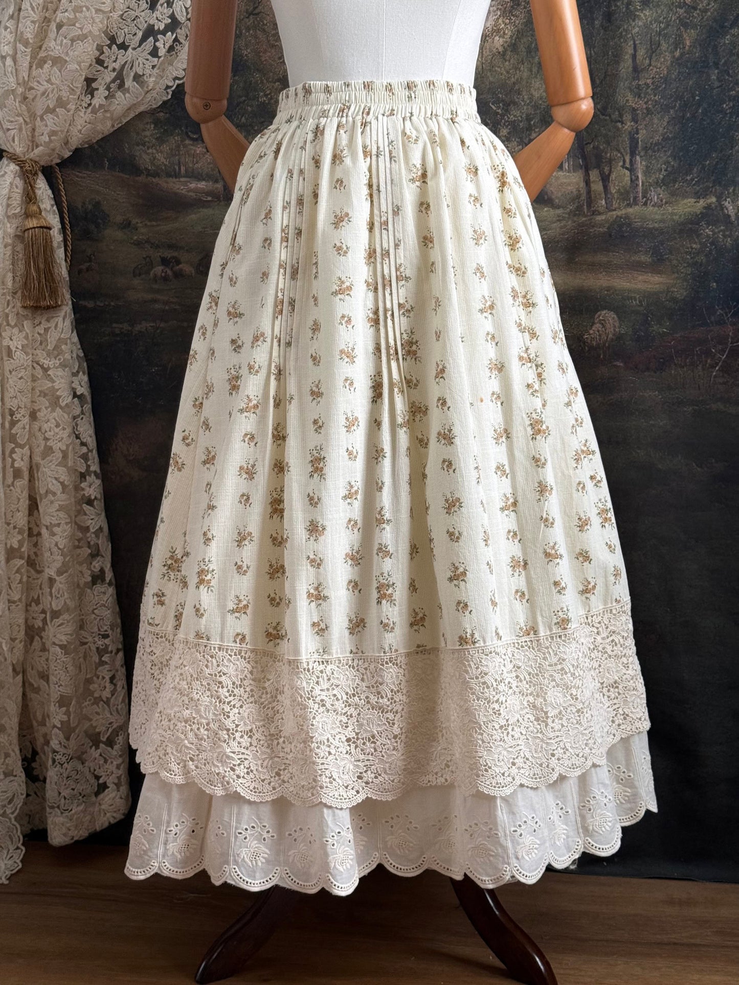 A historically inspired victorian style Ivory cotton floral printed maxi skirt with scalloped lace trim on a mannequin in front of an art history backdrop