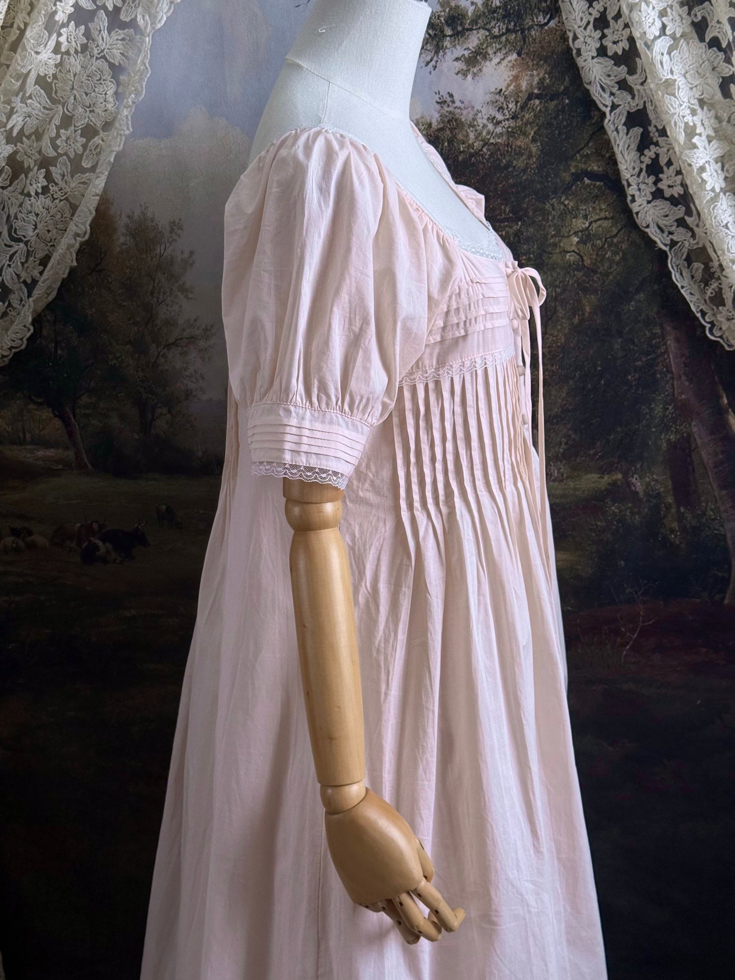 A vintage style historical fashion inspired pastel pink maxi dress with pintuck details and fabric covered buttons, pictured on a mannequin.
