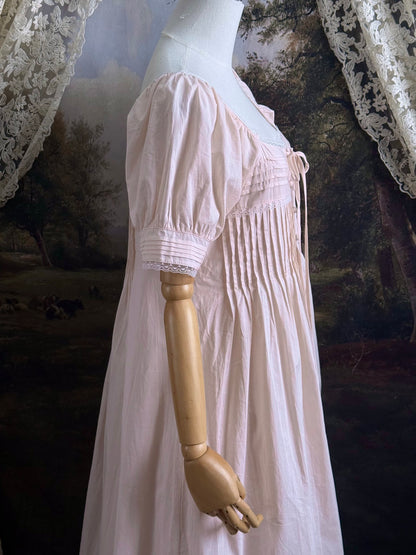 A vintage style historical fashion inspired pastel pink maxi dress with pintuck details and fabric covered buttons, pictured on a mannequin.