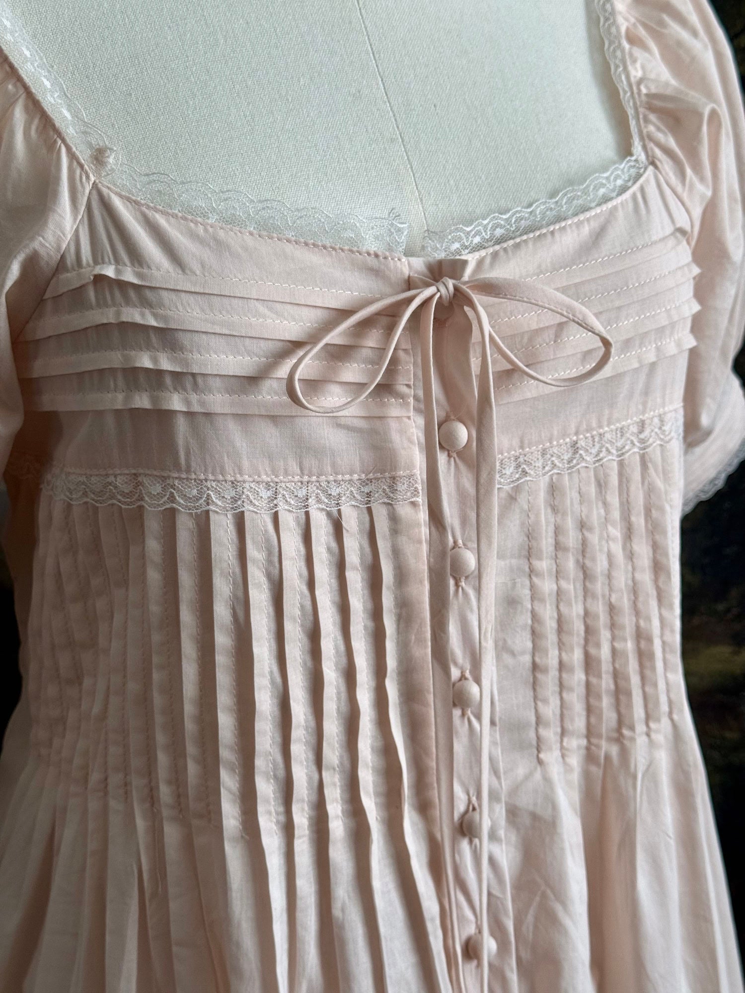 Close-up of the light pink dress with lace details and buttons.