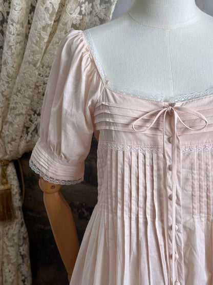 A vintage style historical fashion inspired pastel pink maxi dress with pintuck details and fabric covered buttons, pictured on a mannequin. Close up of sleeve.