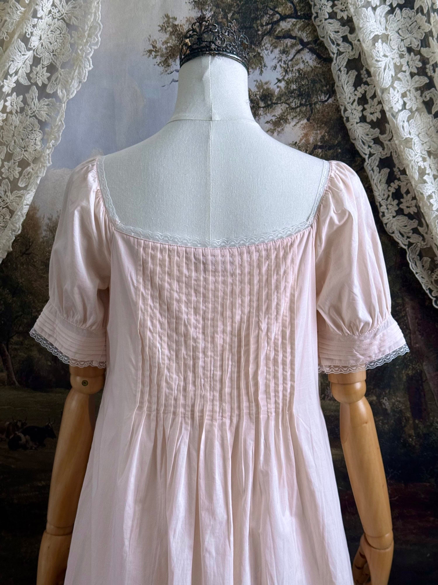 A vintage style historical fashion inspired pastel pink maxi dress with pintuck details and fabric covered buttons, pictured on a mannequin.