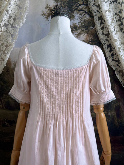 A vintage style historical fashion inspired pastel pink maxi dress with pintuck details and fabric covered buttons, pictured on a mannequin.