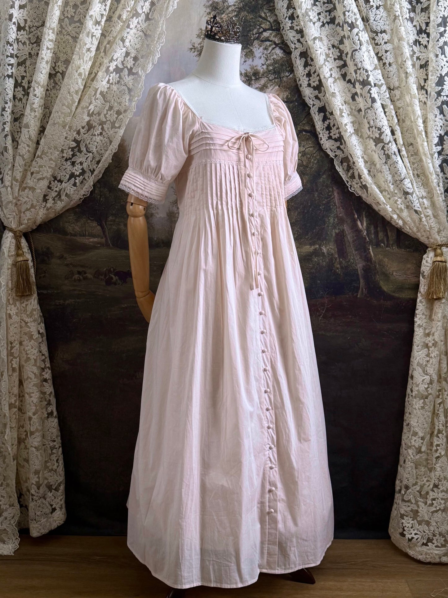 A vintage style historical fashion inspired pastel pink maxi dress with pintuck details and fabric covered buttons, pictured on a mannequin.