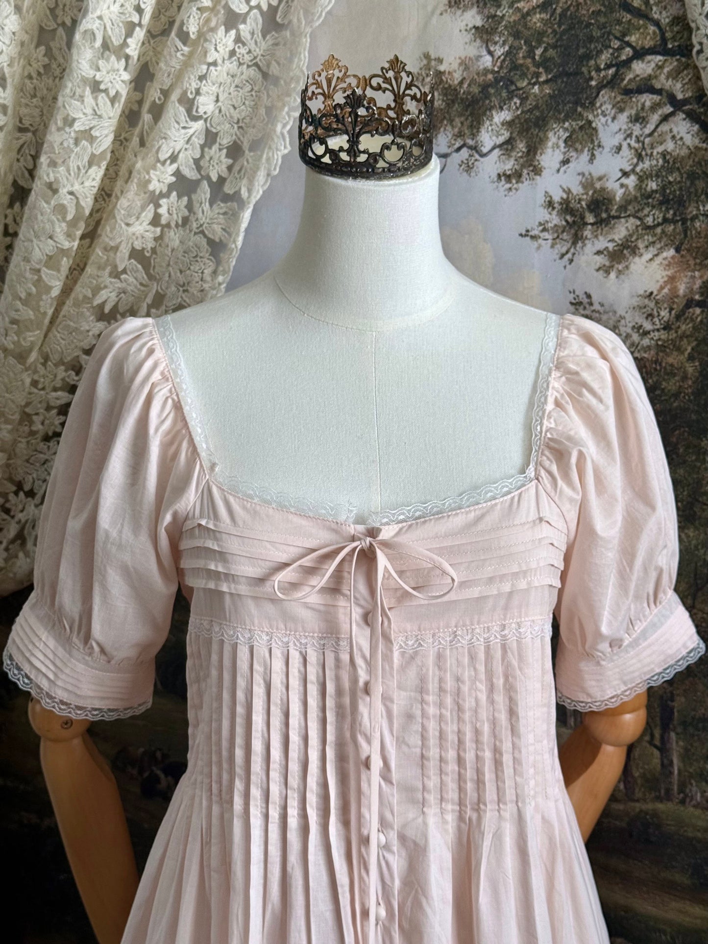 A vintage style historical fashion inspired pastel pink maxi dress with pintuck details and fabric covered buttons, pictured on a mannequin. Close up of bodice.