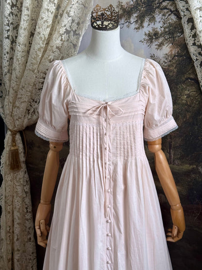 A vintage style historical fashion inspired pastel pink maxi dress with pintuck details and fabric covered buttons, pictured on a mannequin.