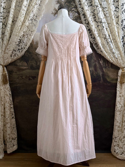 A vintage style historical fashion inspired pastel pink maxi dress with pintuck details and fabric covered buttons, pictured on a mannequin.