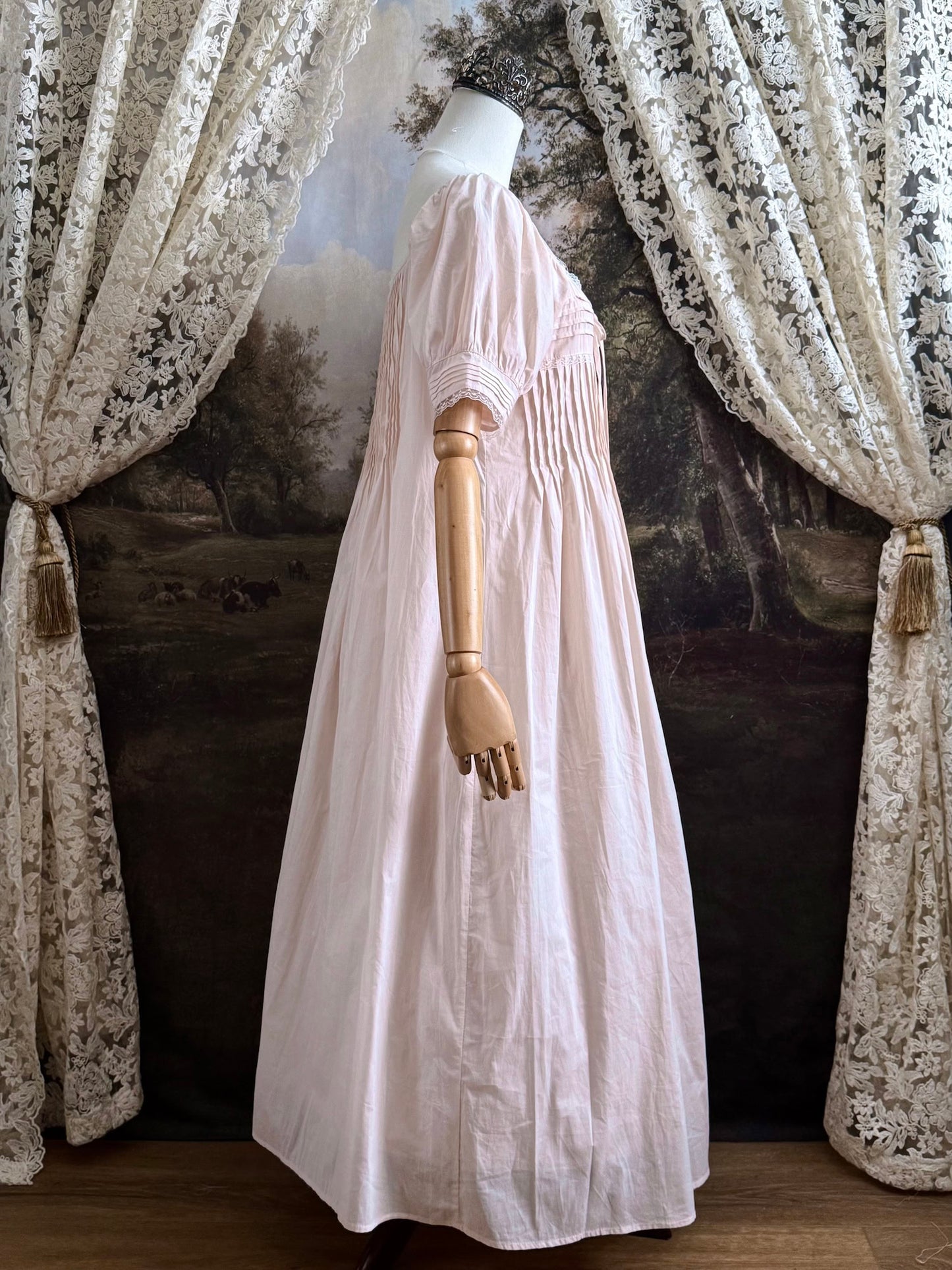A vintage style historical fashion inspired pastel pink maxi dress with pintuck details and fabric covered buttons, pictured on a mannequin.