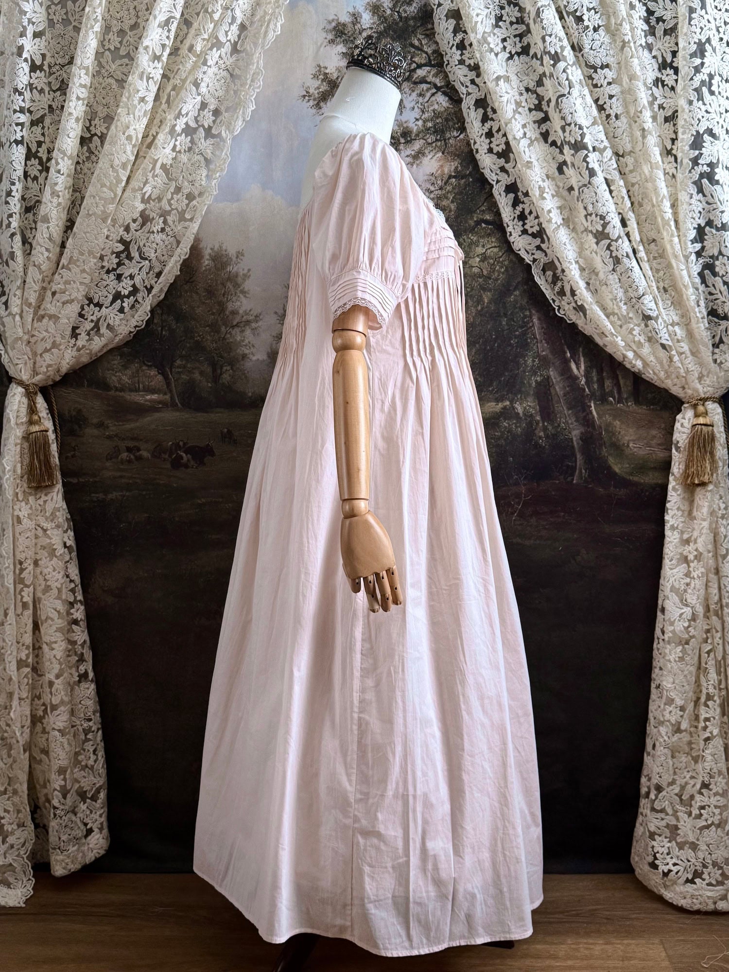A vintage style historical fashion inspired pastel pink maxi dress with pintuck details and fabric covered buttons, pictured on a mannequin.