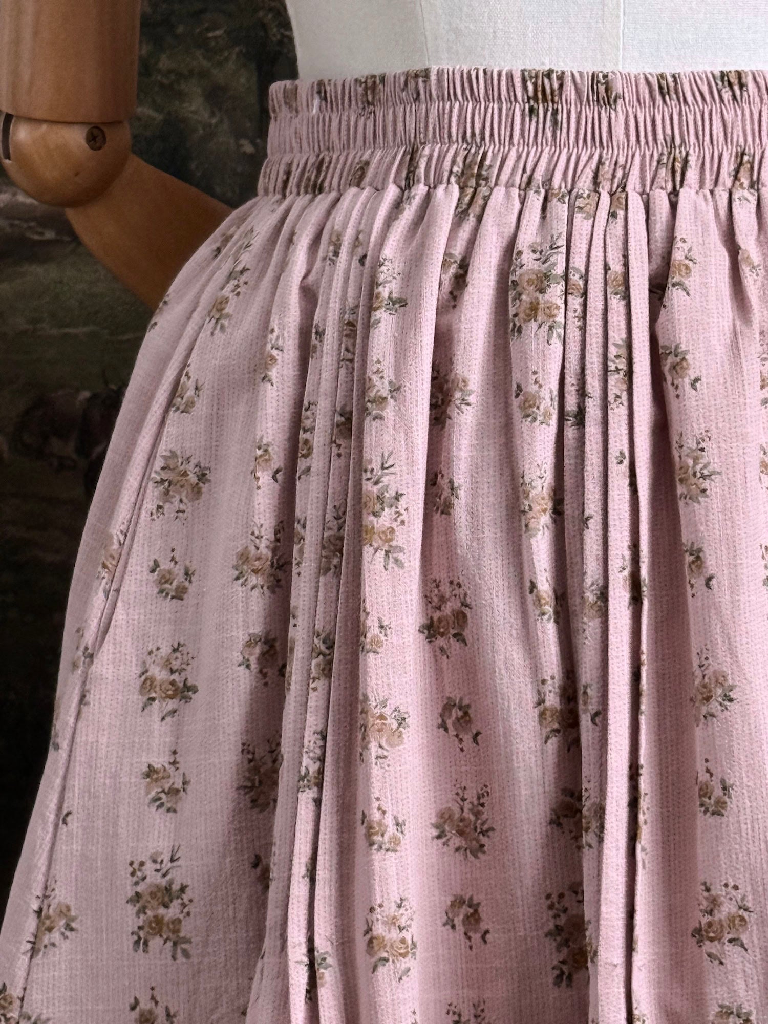 A vintage style historical fashion inspire floral print cotton skirt in mauve with scalloped floral lace trim, pictured on a mannequin in front of a historical painting backdrop.