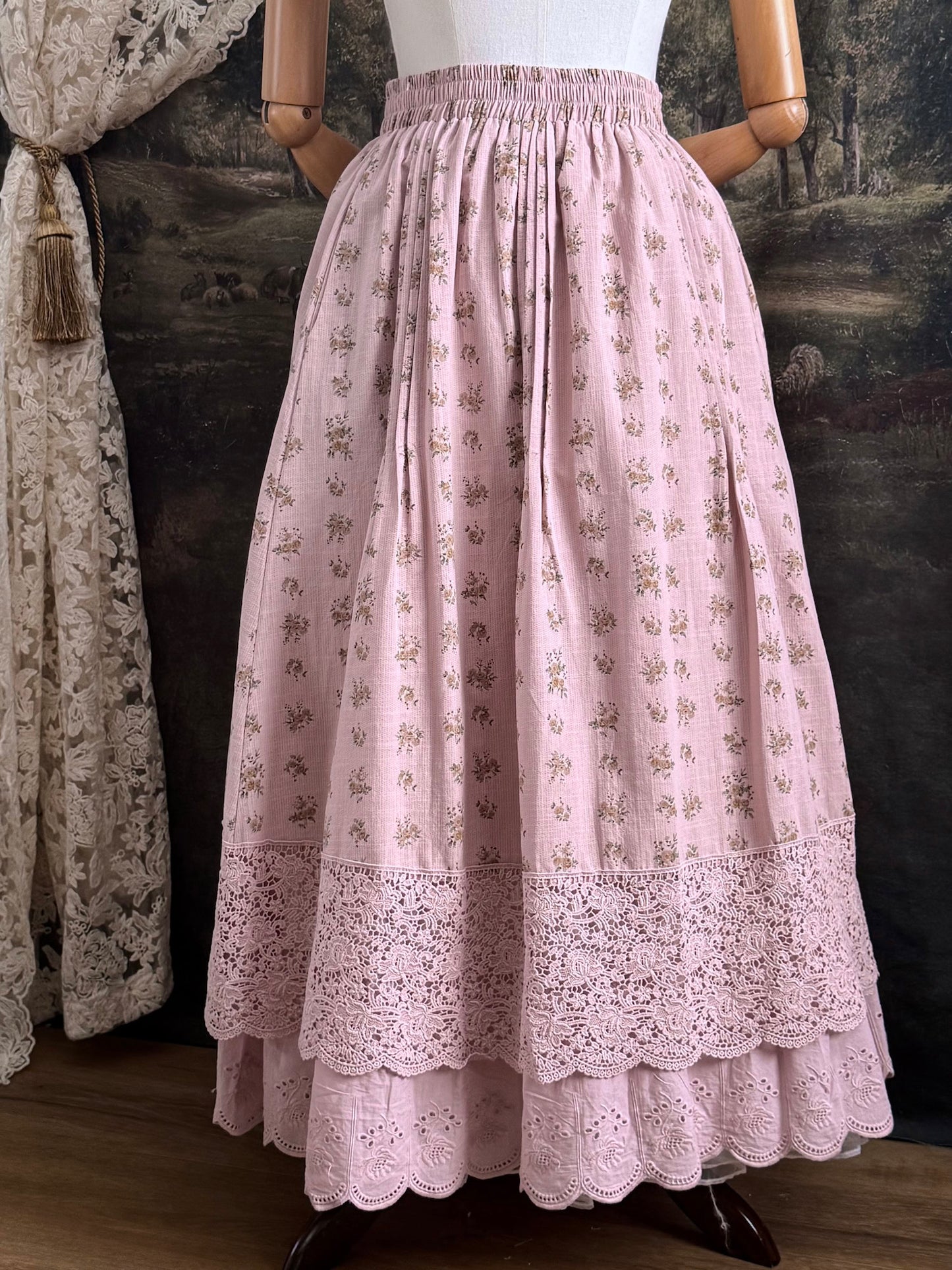 A vintage style historical fashion inspire floral print cotton skirt in mauve with scalloped floral lace trim, pictured on a mannequin in front of a historical painting backdrop.