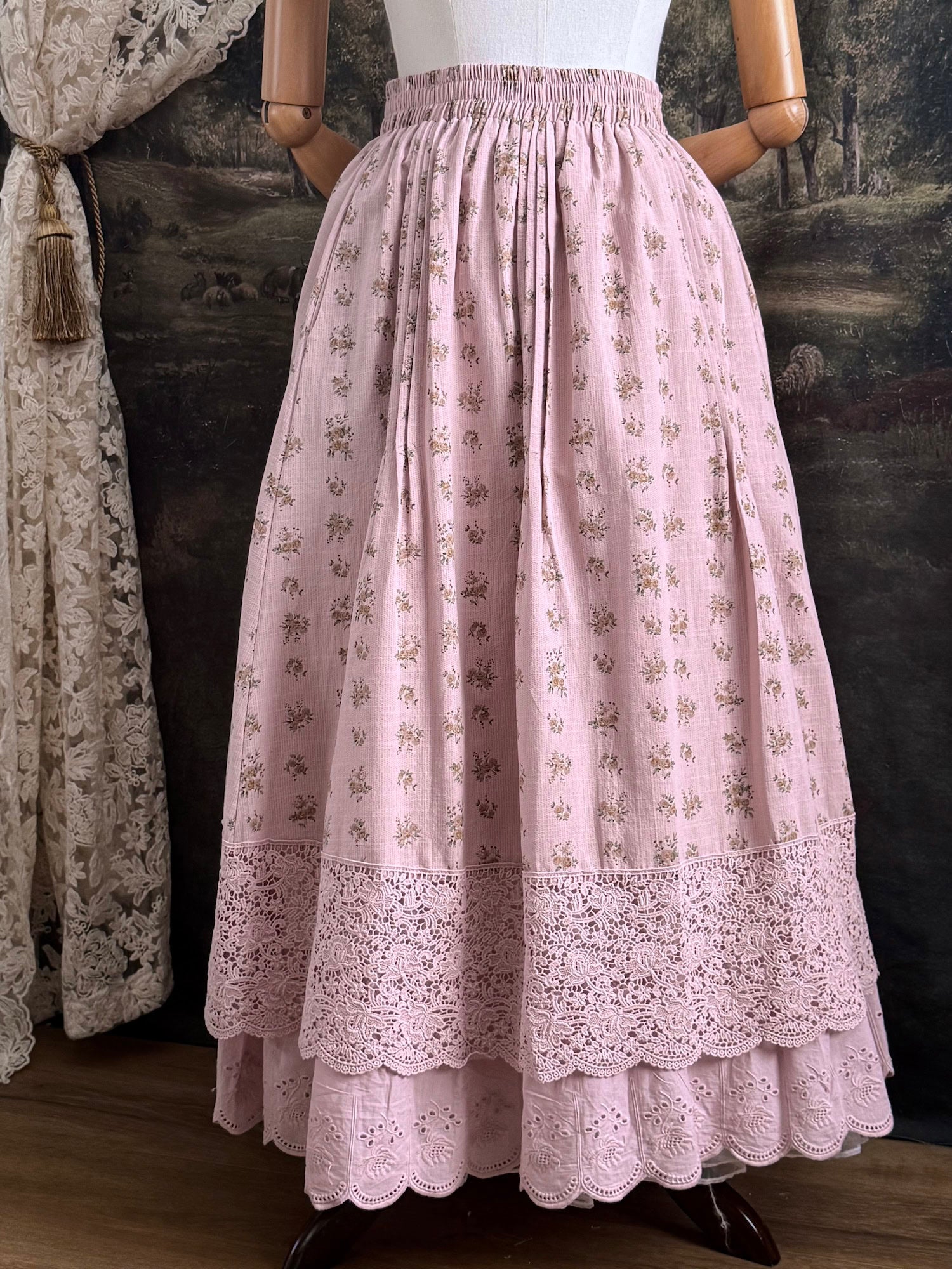 A vintage style historical fashion inspire floral print cotton skirt in mauve with scalloped floral lace trim, pictured on a mannequin in front of a historical painting backdrop.