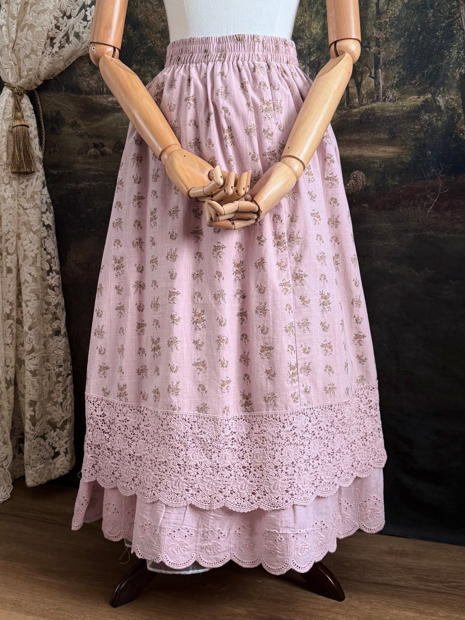 A vintage style historical fashion inspire floral print cotton skirt in mauve with scalloped floral lace trim, pictured on a mannequin in front of a historical painting backdrop.