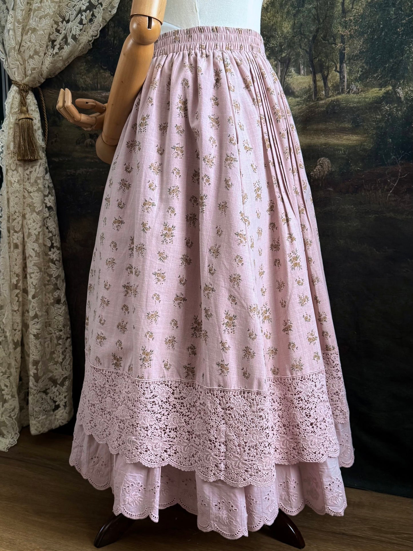 A vintage style historical fashion inspire floral print cotton skirt in mauve with scalloped floral lace trim, pictured on a mannequin in front of a historical painting backdrop.