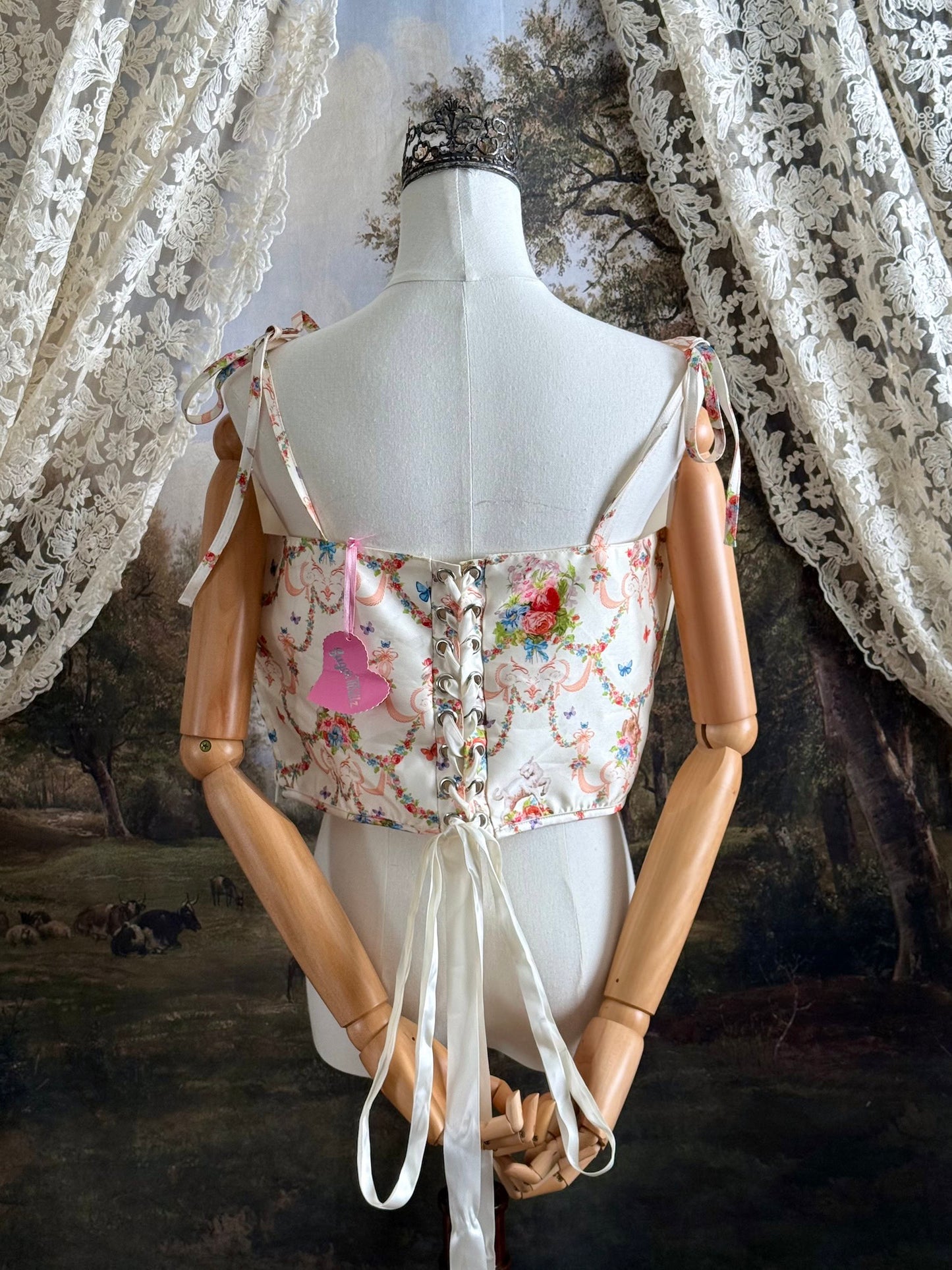 A historically-inspired 1700s rococo era corset top in an ivory floral printed satin is pictured on a mannequin in front of an art history backdrop.