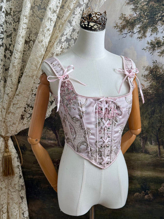 Historical fashion inspired baroque to rococo era front-laced corset stays top in pastel pink floral jacquard fabric, pictured on a mannequin.