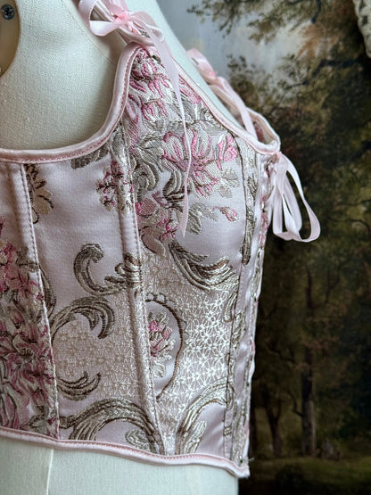 Historical fashion inspired baroque to rococo era front-laced corset stays top in pastel pink floral jacquard fabric, pictured on a mannequin.