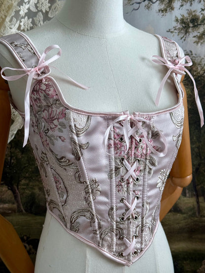 Historical fashion inspired baroque to rococo era front-laced corset stays top in pastel pink floral jacquard fabric, pictured on a mannequin.