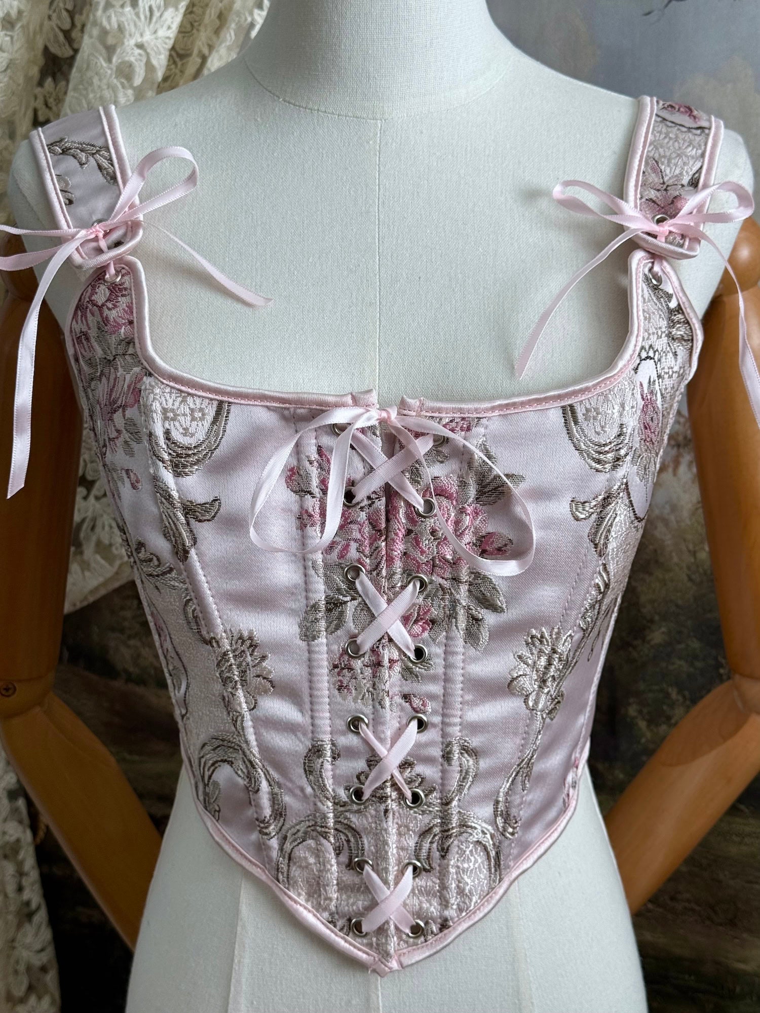 Historical fashion inspired baroque to rococo era front-laced corset stays top in pastel pink floral jacquard fabric, pictured on a mannequin.