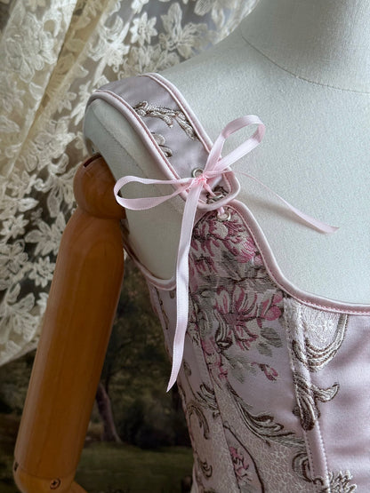 Historical fashion inspired baroque to rococo era front-laced corset stays top in pastel pink floral jacquard fabric, pictured on a mannequin. Detail of ribbons.