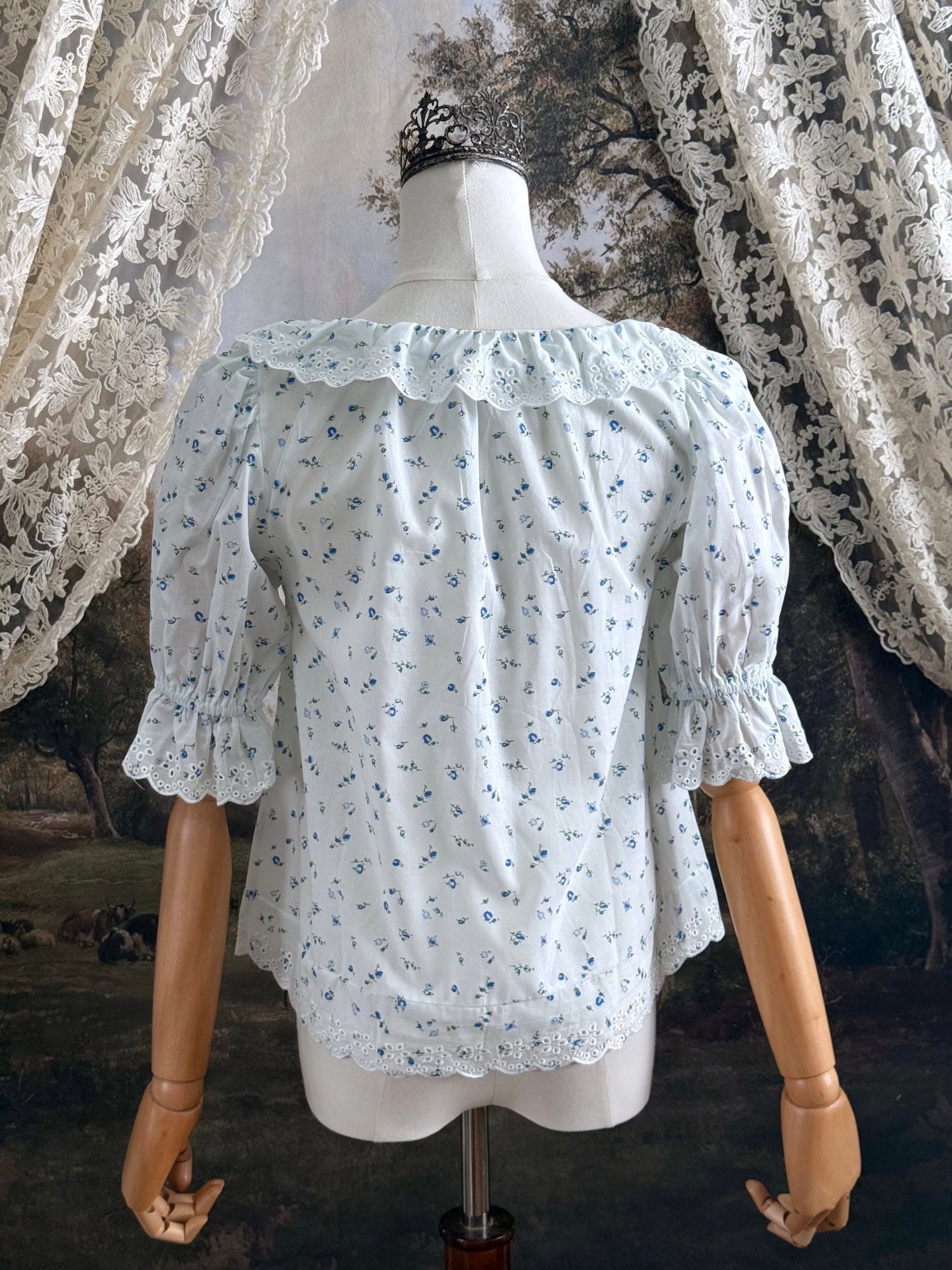 A vintage style historically-inspired white and blue floral print cotton button-up blouse with scalloped lace collar and trim, pictured on a mannequin.