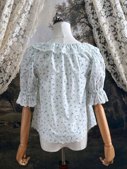 A vintage style historically-inspired white and blue floral print cotton button-up blouse with scalloped lace collar and trim, pictured on a mannequin.