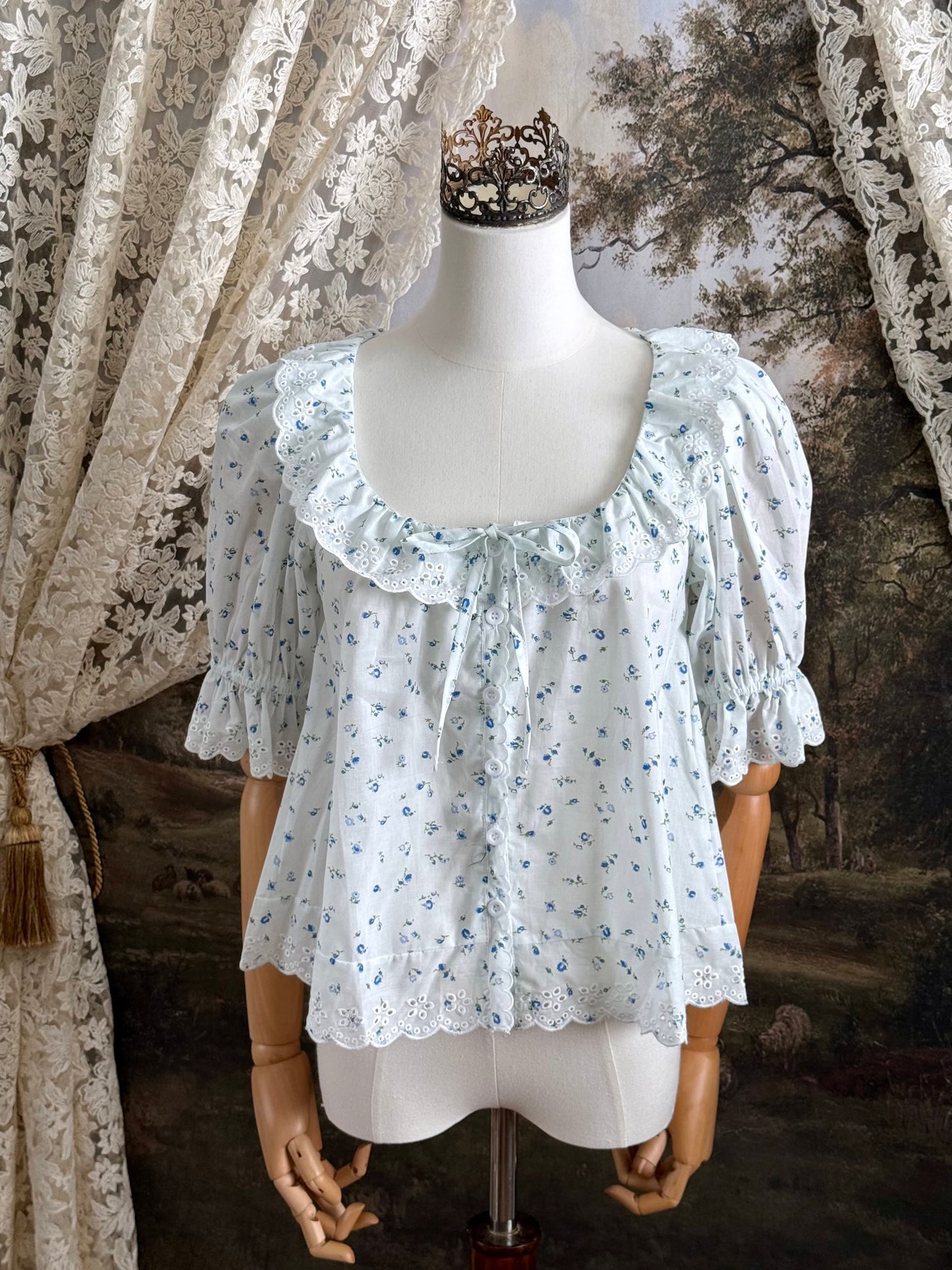 A vintage style historically-inspired white and blue floral print cotton button-up blouse with scalloped lace collar and trim, pictured on a mannequin.