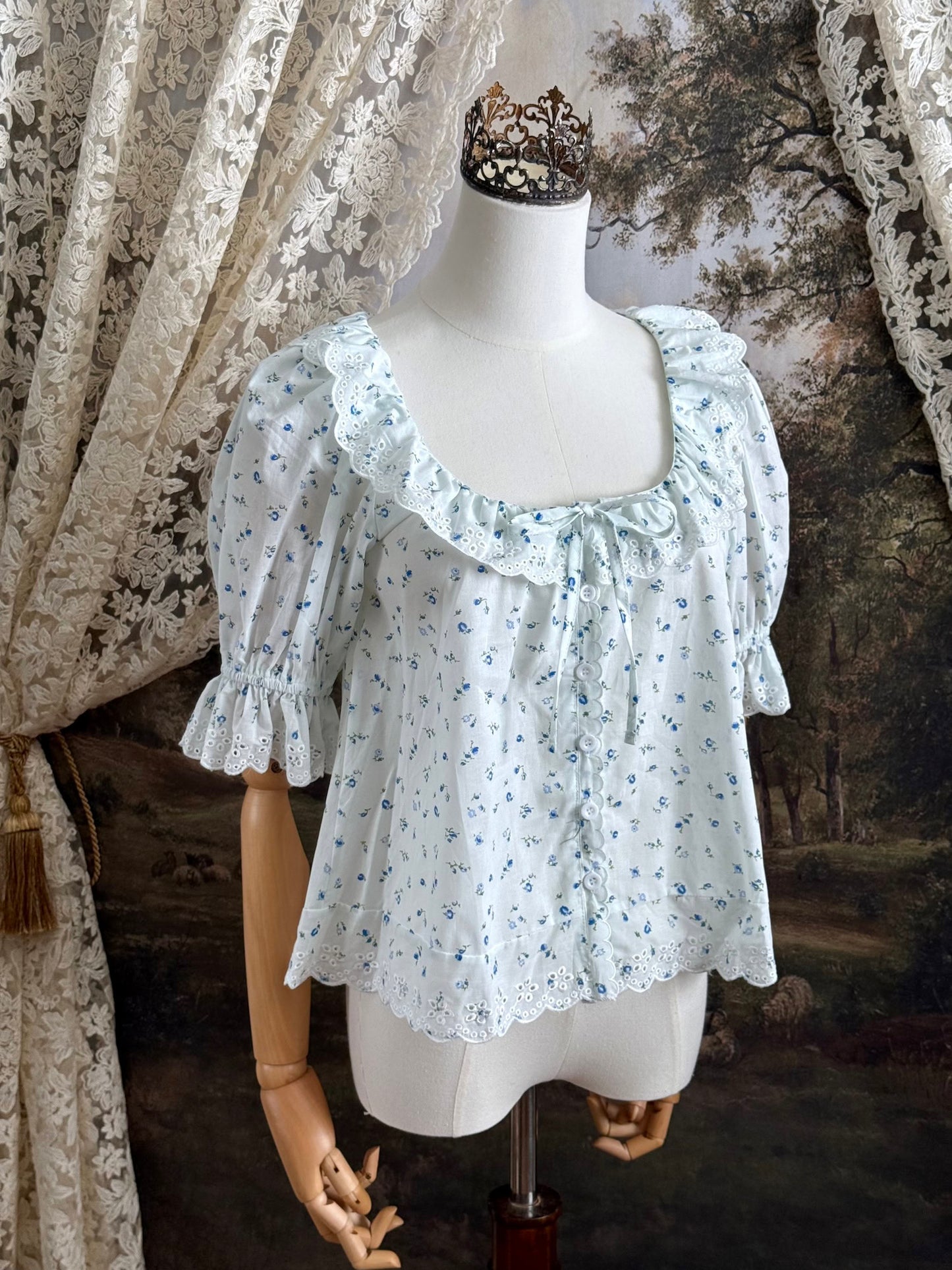 A vintage style historically-inspired white and blue floral print cotton button-up blouse with scalloped lace collar and trim, pictured on a mannequin.