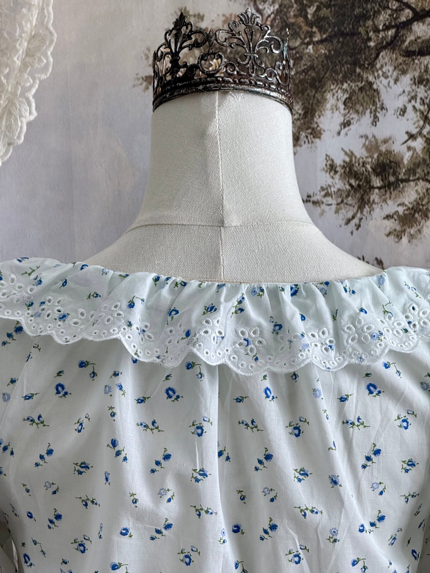 A vintage style historically-inspired white and blue floral print cotton button-up blouse with scalloped lace collar and trim, pictured on a mannequin.