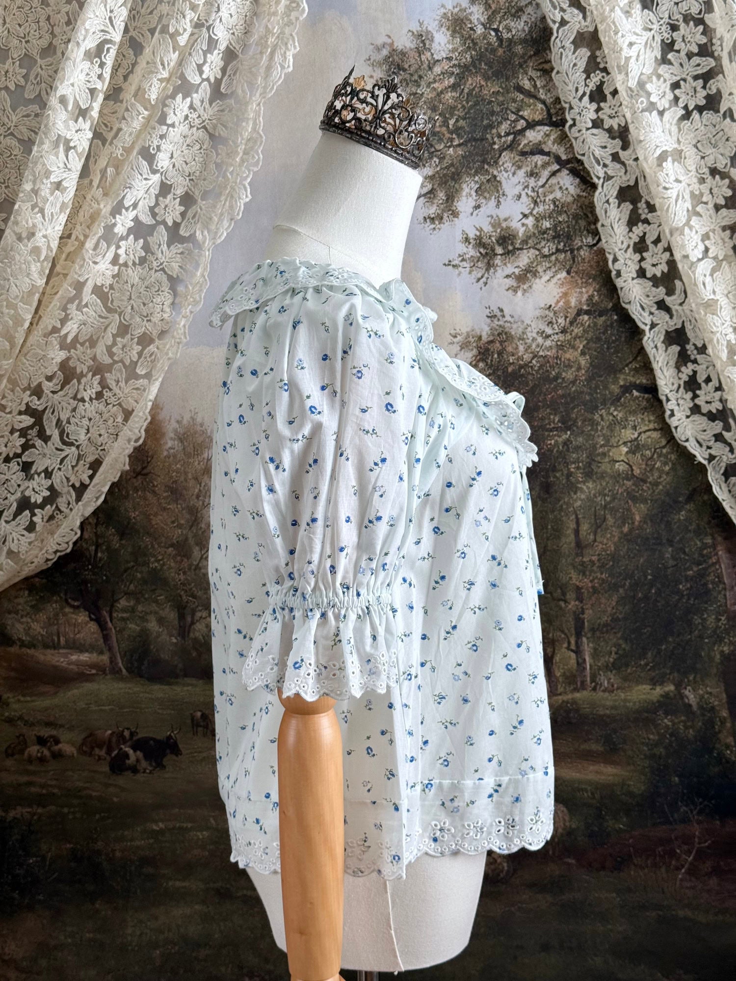 A vintage style historically-inspired white and blue floral print cotton button-up blouse with scalloped lace collar and trim, pictured on a mannequin.