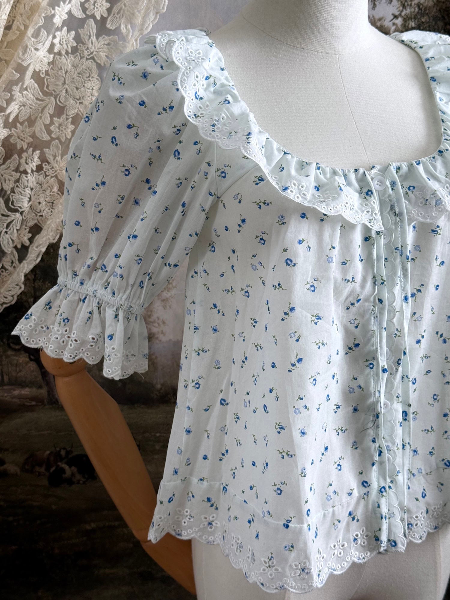 A vintage style historically-inspired white and blue floral print cotton button-up blouse with scalloped lace collar and trim, pictured on a mannequin.