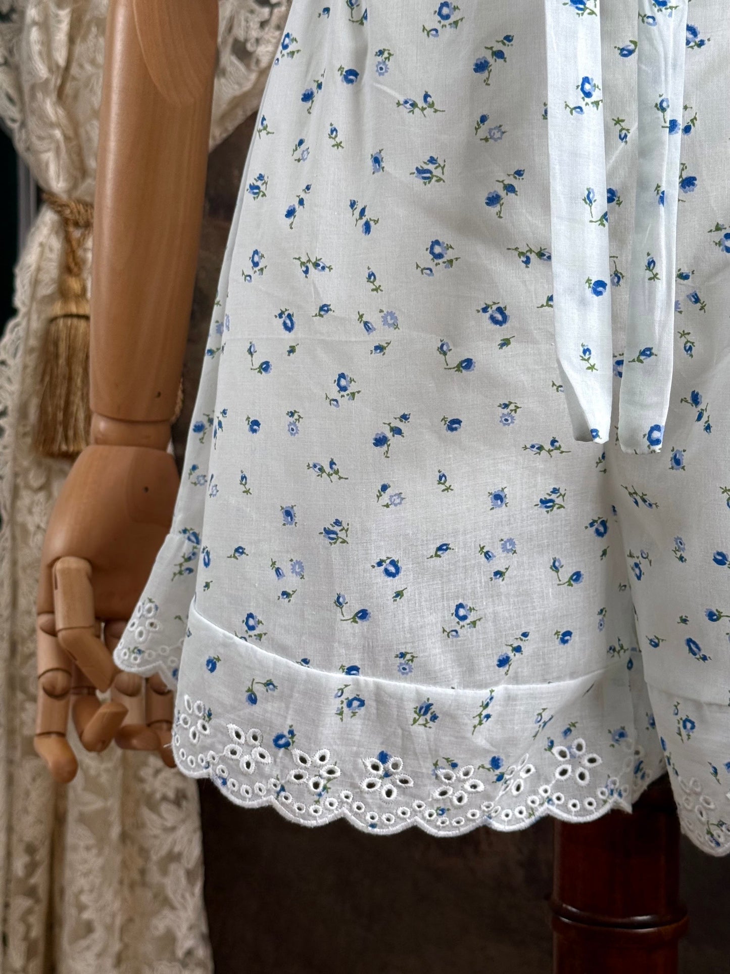 A pair of vintage inspired white and blue floral print cotton bloomer shorts with scalloped lace trim and bow-tied waist drawstring, pictured on a mannequin.