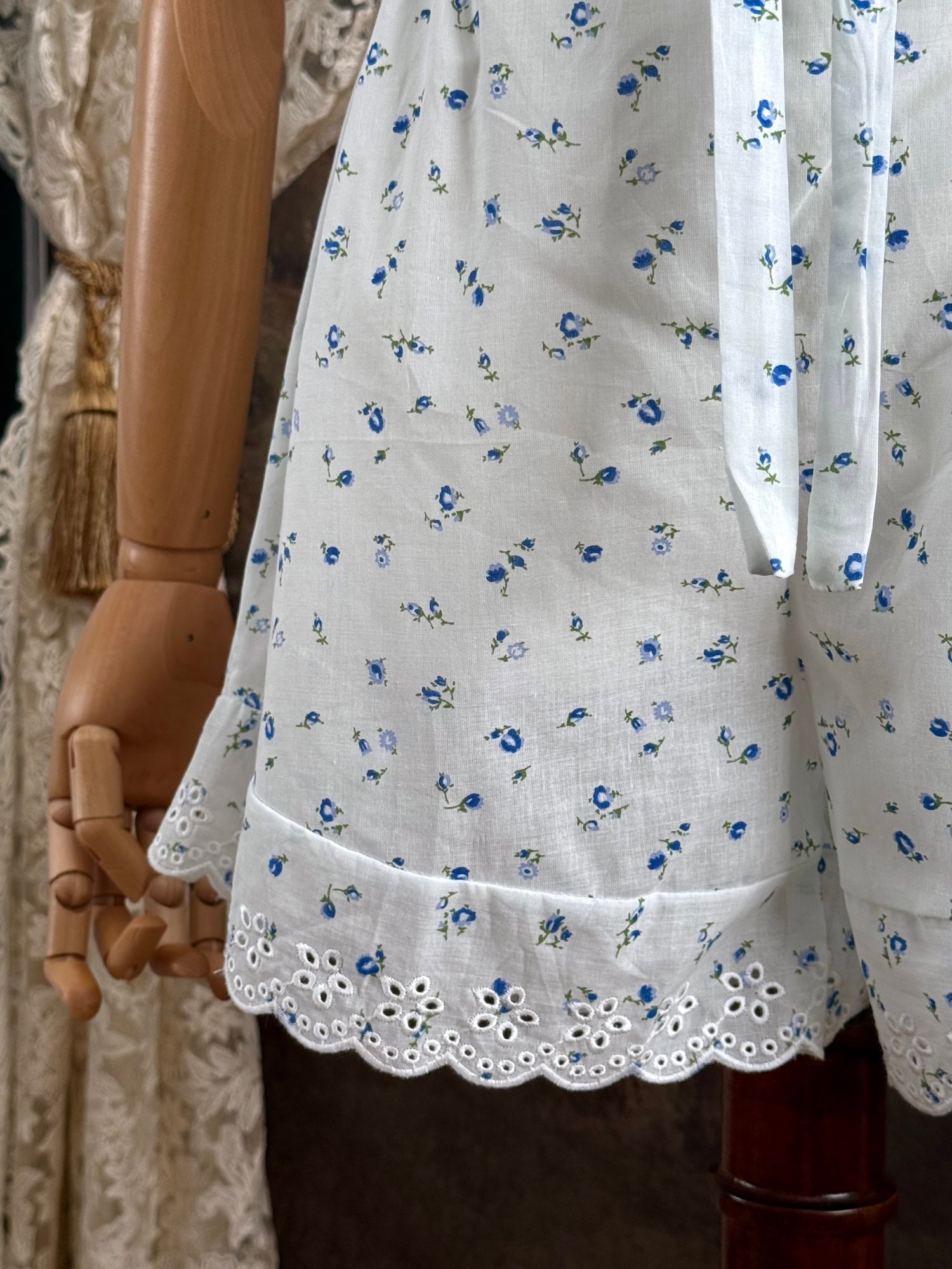 A pair of vintage inspired white and blue floral print cotton bloomer shorts with scalloped lace trim and bow-tied waist drawstring, pictured on a mannequin.