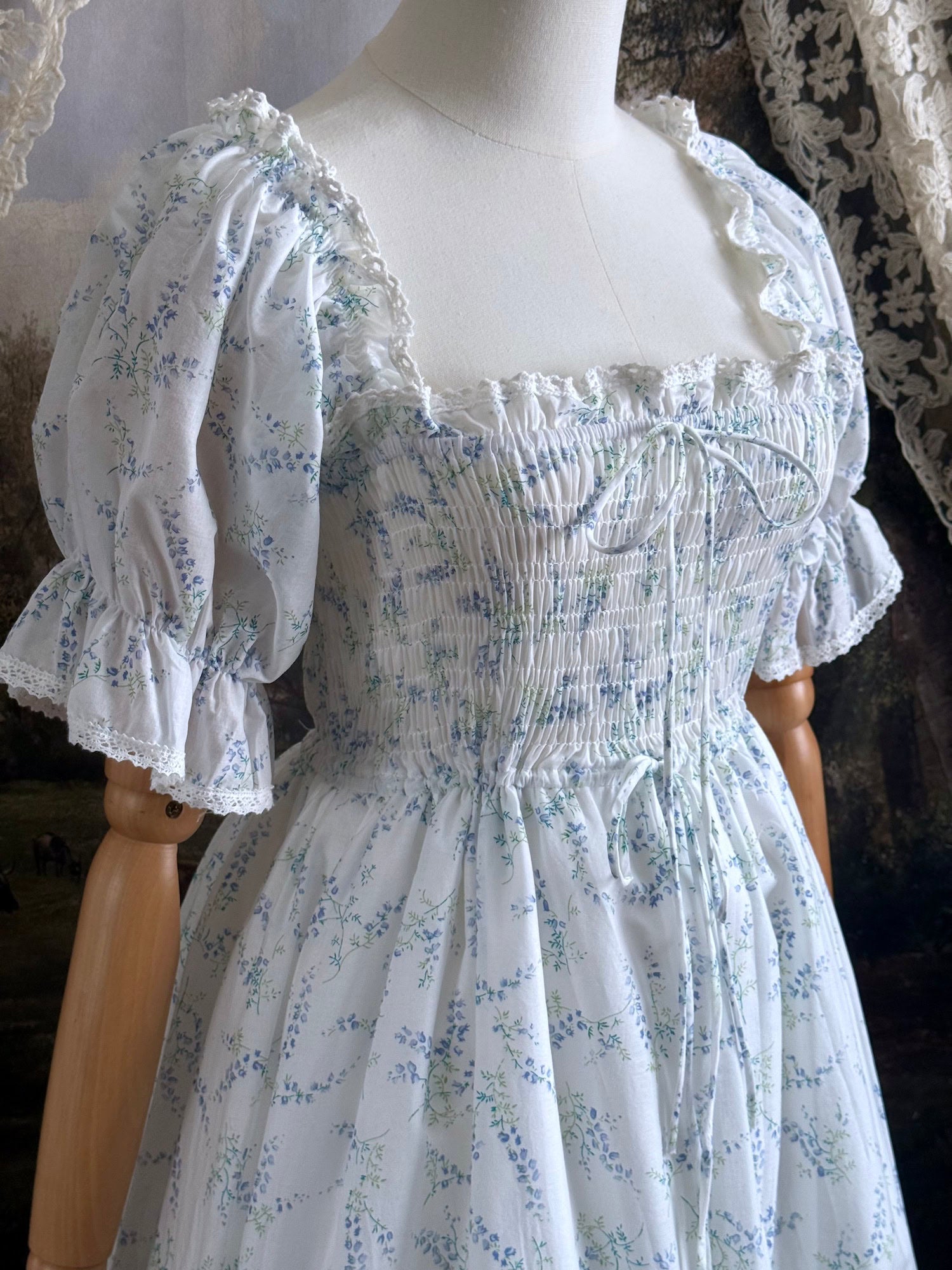 A Historically Inspired regency style puff sleeve White Floral Print Cotton Chemise maxi Dress with Shirred bodice, drawstring cinching laces, and lace trim up close.