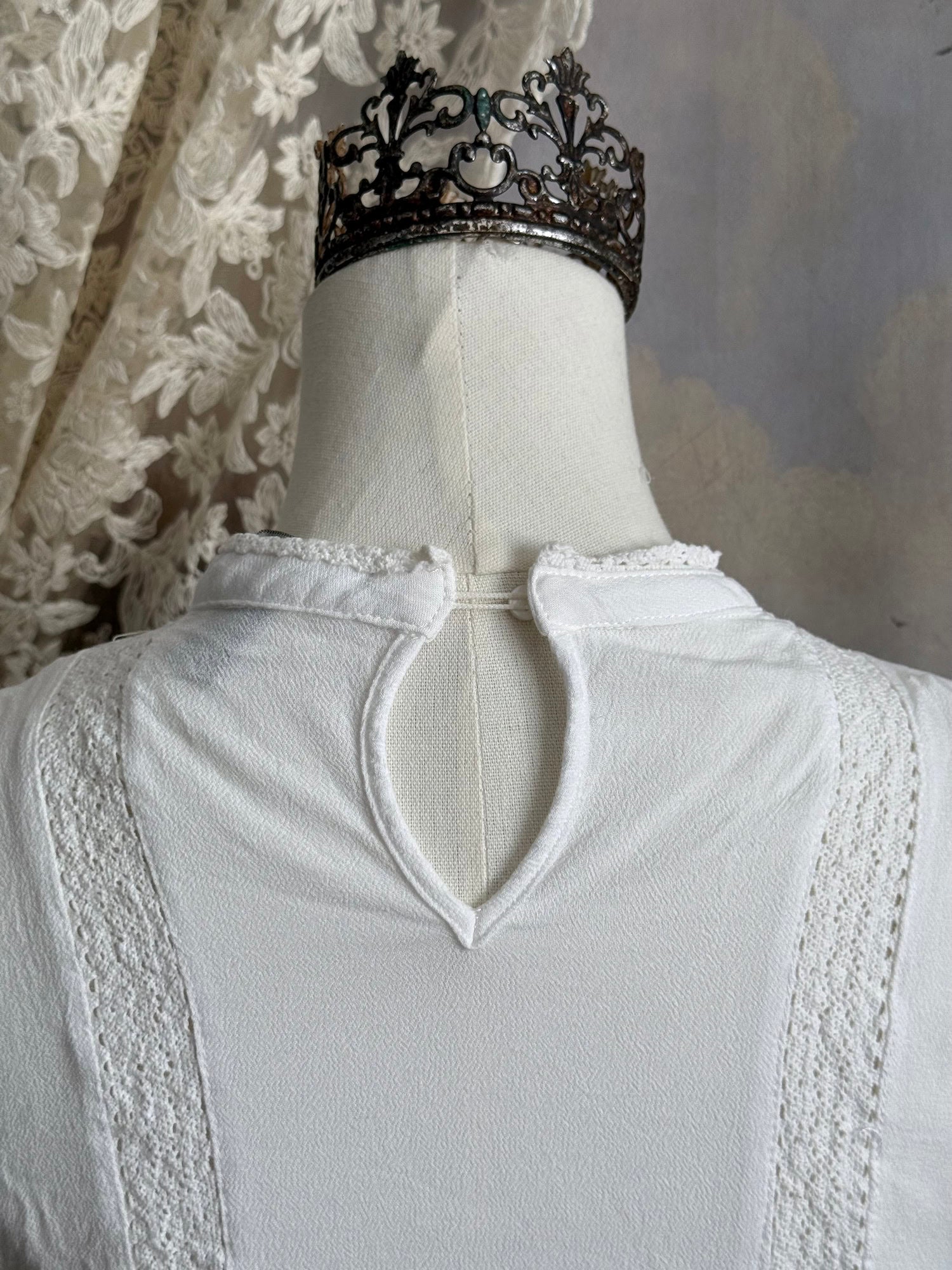 White edwardian-inspired sleeveless tank top blouse with floral embroidery and lace trim details, pictured on a mannequin against an art history background.
