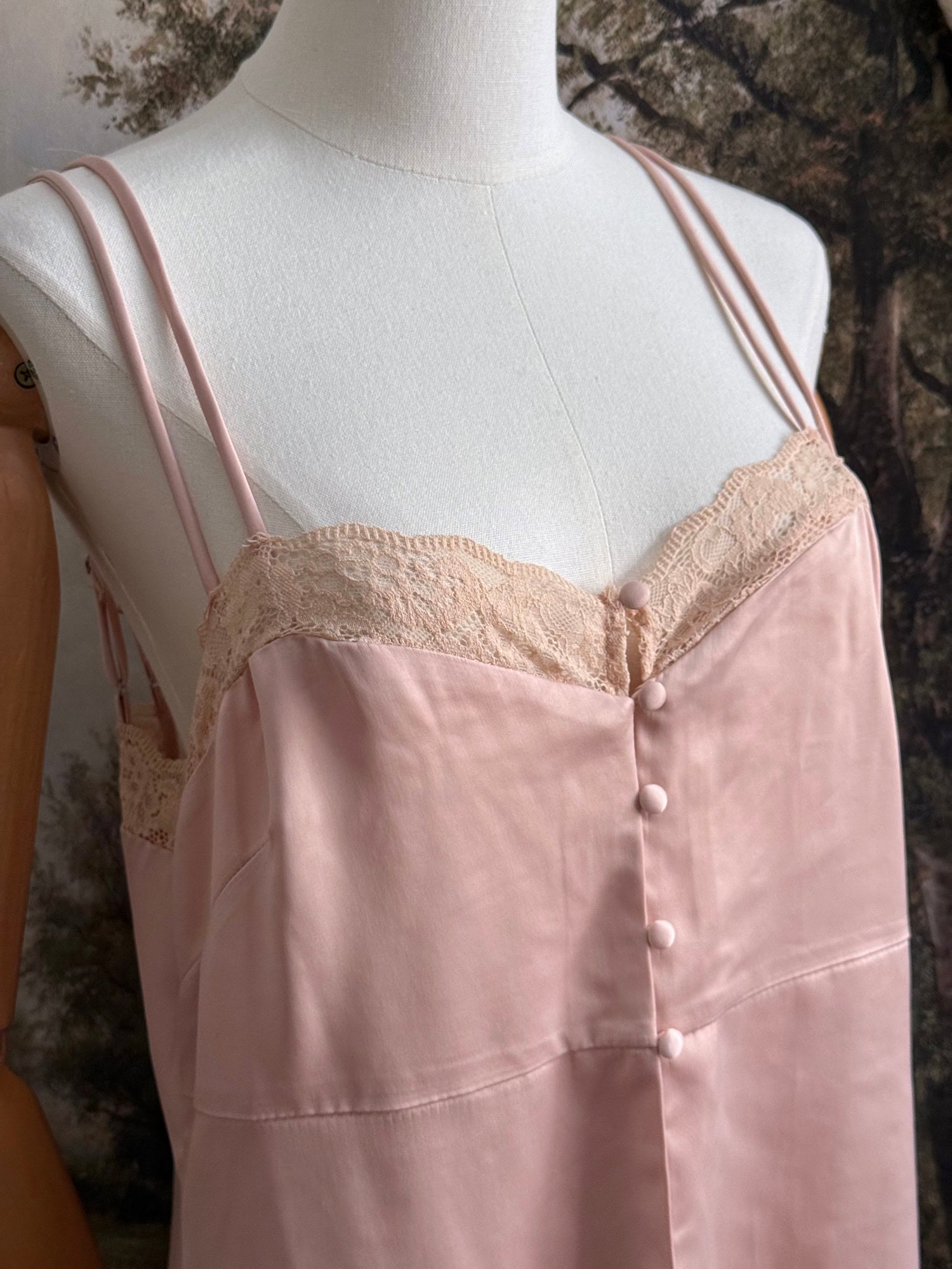 A historically inspired vintage style peachy pink satin overdress with covered buttons and lace trim on a mannequin