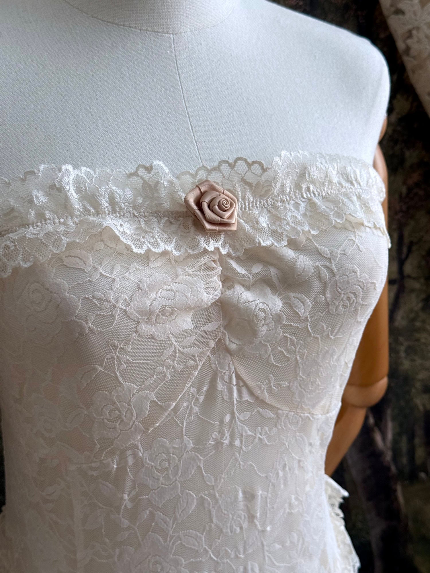 A victorian-inspired lacy chiffon overdress with ruffle lace trim and rosette appliques, pictured on a mannequin in front of a historical painted backdrop.