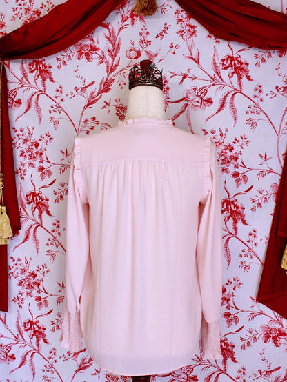 A historically inspired victorian style pastel pink long bishop sleeve blouse with smocked yoke and cuffs in front of a toile backdrop.