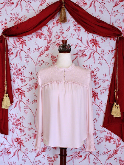 A historically inspired victorian style pastel pink long bishop sleeve blouse with smocked yoke and cuffs in front of a toile backdrop.