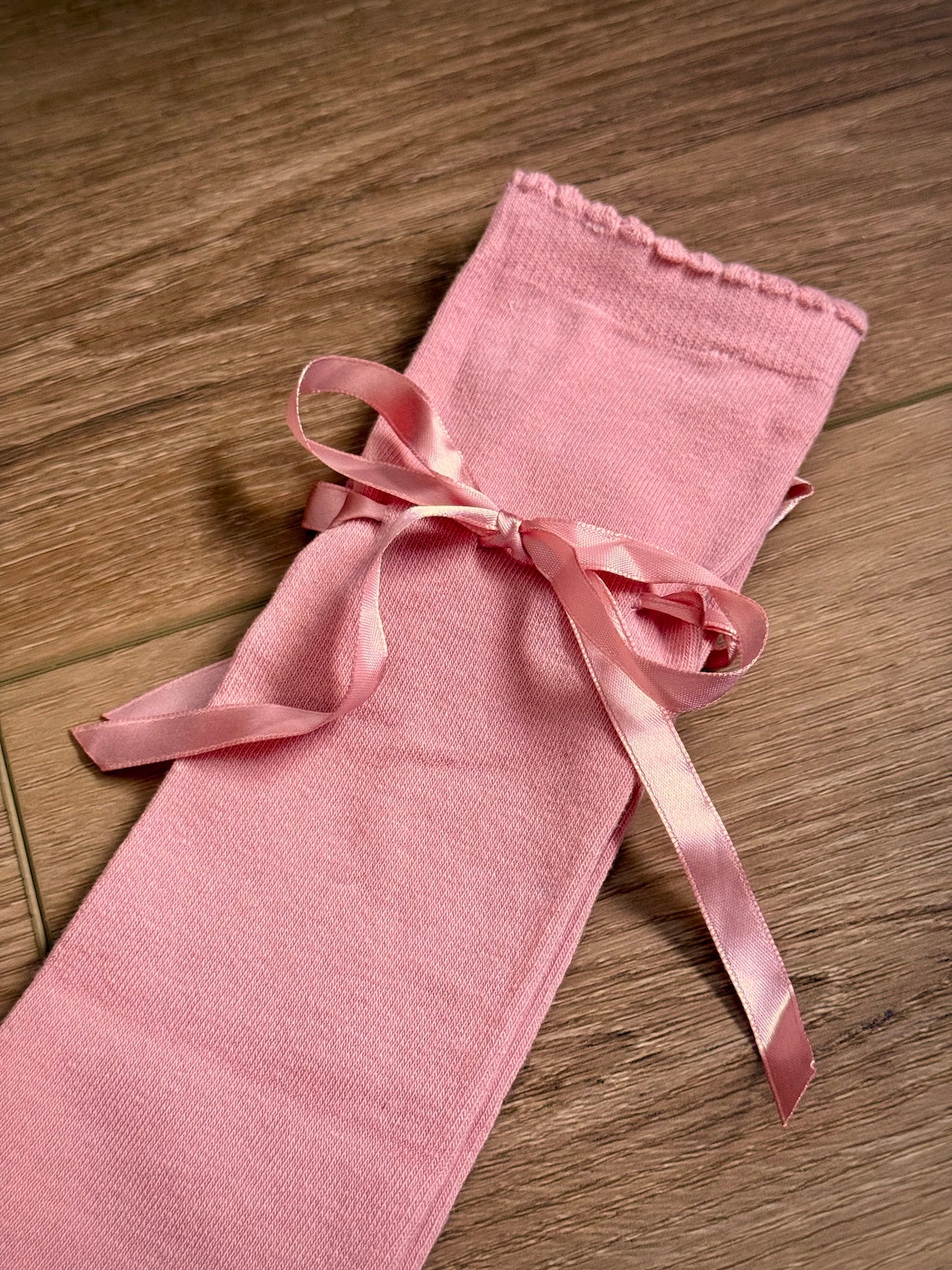 Details of historically inspired knee high stocking socks in a peach ballerina pink, laying on a wooden cottage floor. For edwardian, victorian, regency, rococo, baroque, renaissance, and medieval era fashion.
