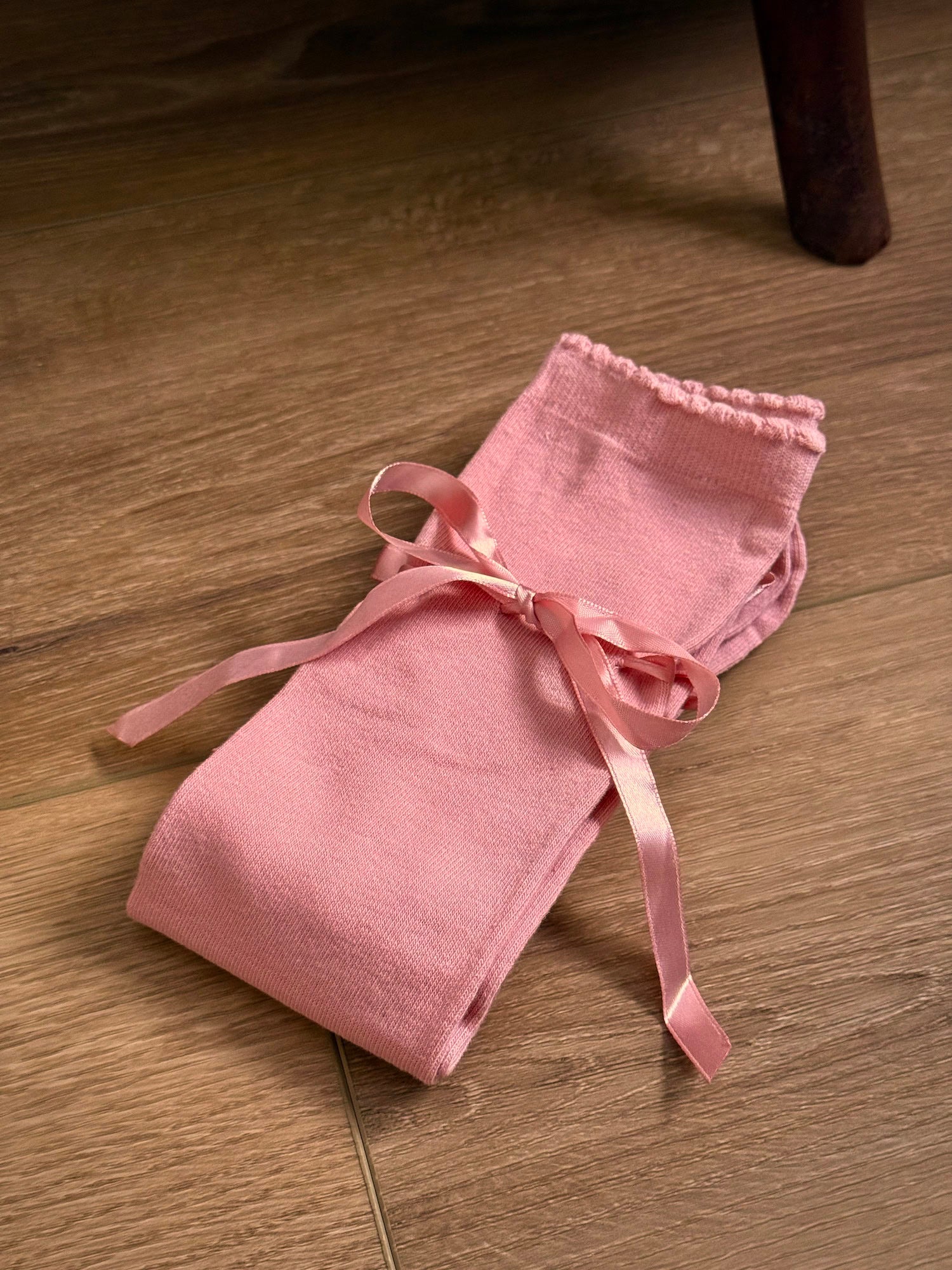 A pair of historically inspired knee high stocking socks in a peach ballerina pink, laying folded on a wooden cottage floor. For edwardian, victorian, regency, rococo, baroque, renaissance, and medieval era fashion.