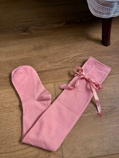 A pair of historically inspired knee high stocking socks in a peach ballerina pink, laying on a wooden cottage floor. For edwardian, victorian, regency, rococo, baroque, renaissance, and medieval era fashion.