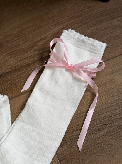 A pair of Historically Inspired Cotton Knee-High Socks with Satin Ribbon Lacing in White and Pink, pictured on a cottagecore wooden floor. For Medieval, Renaissance, Baroque, Rococo, Regency, Victorian, or Edwardian fashion. 