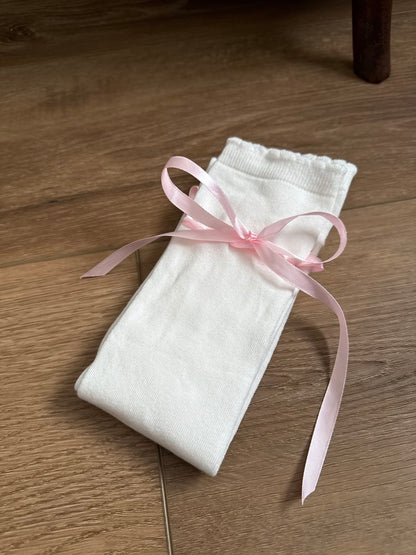A pair of Historically Inspired Cotton Knee-High Socks with Satin Ribbon Lacing in White and Pink, pictured on a cottagecore wooden floor. For Medieval, Renaissance, Baroque, Rococo, Regency, Victorian, or Edwardian fashion. 