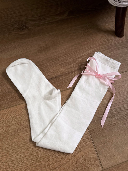 A pair of Historically Inspired Cotton Knee-High Socks with Satin Ribbon Lacing in White and Pink, pictured on a cottagecore wooden floor. For Medieval, Renaissance, Baroque, Rococo, Regency, Victorian, or Edwardian fashion. 